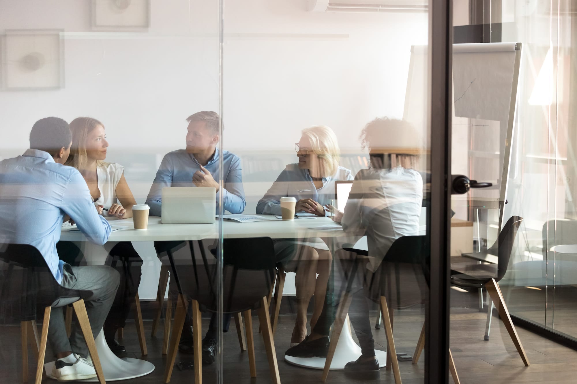 A group of business people in a marketing meeting taking place in a glass conference room.